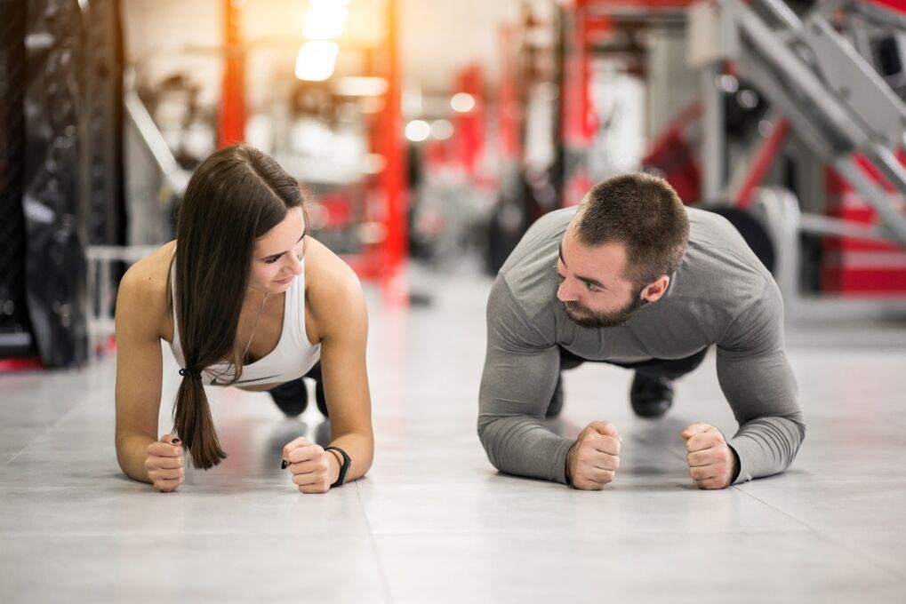 A man and a woman perform the Plank exercise, designed for all muscle groups